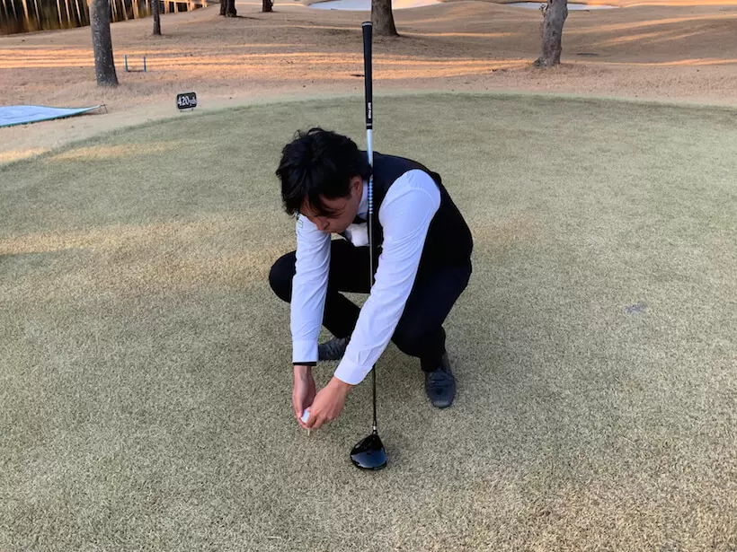 ゴルフ場での今野さんの写真,ボールを持ってしゃがみ込む
