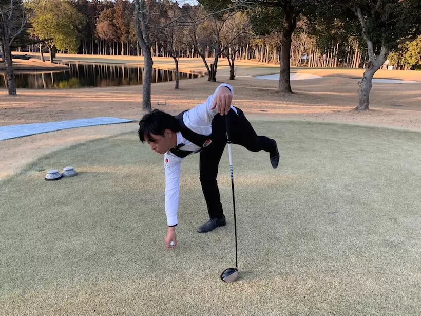 ゴルフ場での今野さんの写真,ボールを持ちながら立ち上がり片足上げている