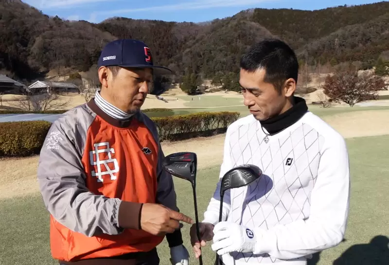 ゴルフ場で野村タケオと佐藤順がクラブを持って話している写真
