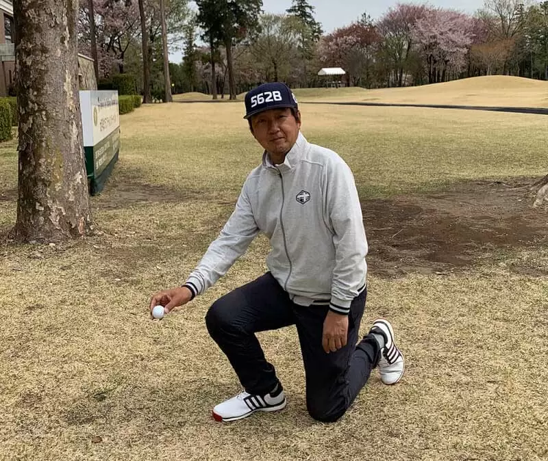 ゴルフ場で野村タケオが片膝をついてドロップしようとする写真