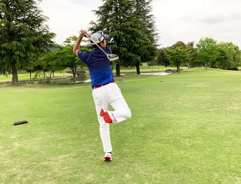 ゴルフ場で打っている後ろ姿,右足が後ろに蹴りあがっている