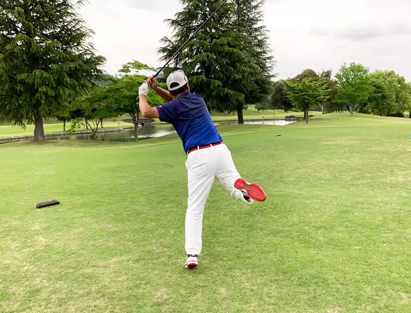 ゴルフ場で打っている後ろ姿,右足が後ろに蹴りあがり身体は左側に傾く