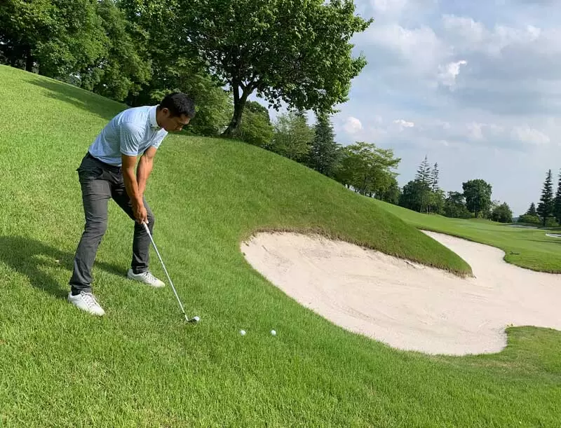 佐藤順が傾斜のあるラフからショットを打つところの写真