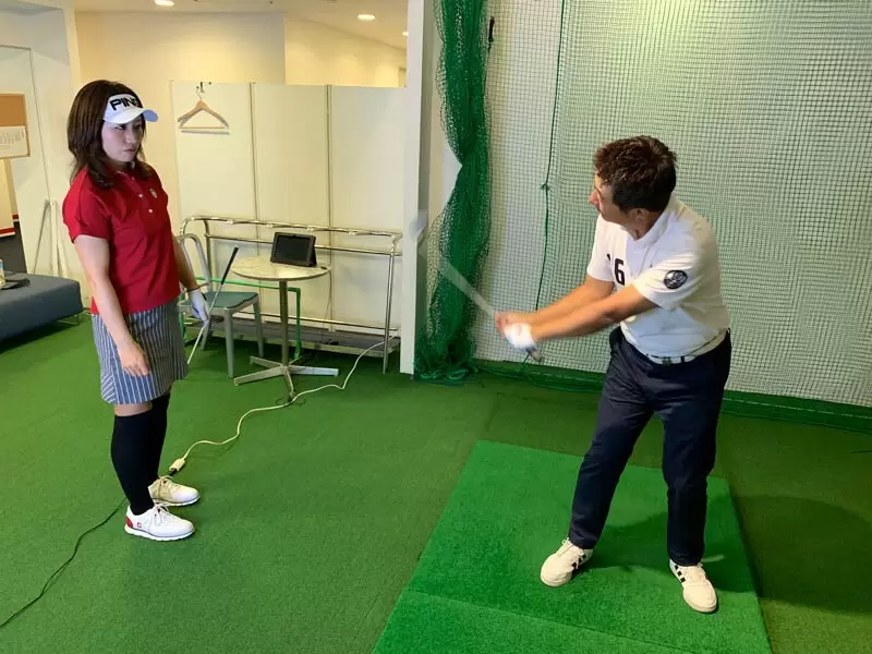 野村タケオが勝又プロから指導を受けている写真,後ろから勝又プロがみている