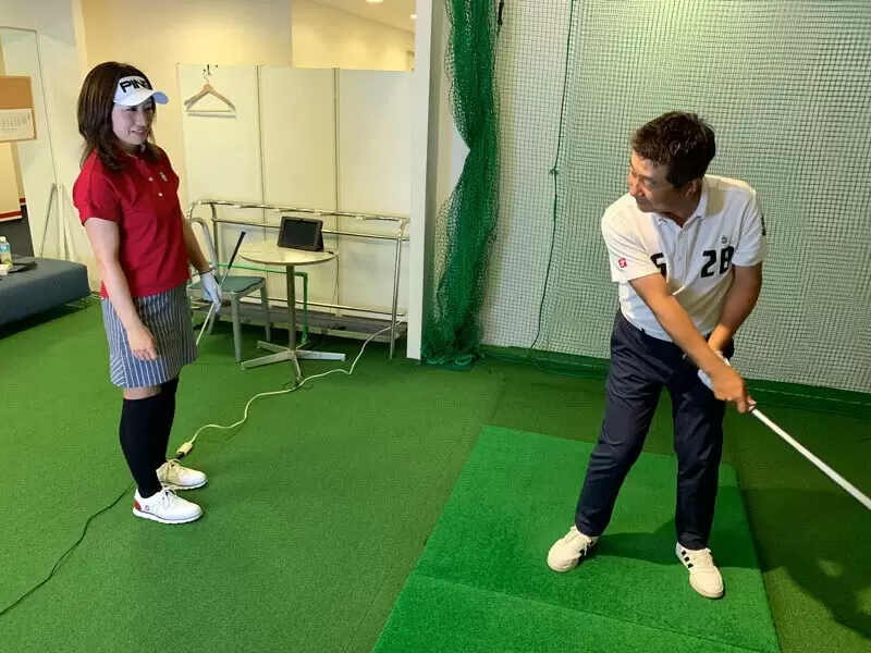 野村タケオが勝又プロから指導を受けている写真,後ろから勝又プロがみている