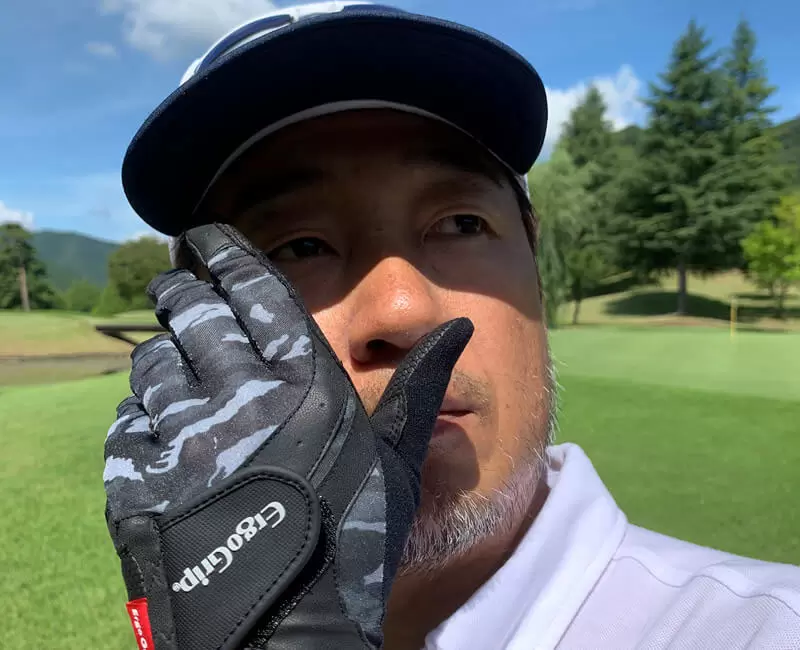 ゴルフ場で野村タケオが指が曲がったグローブを着けてポーズをとっている写真