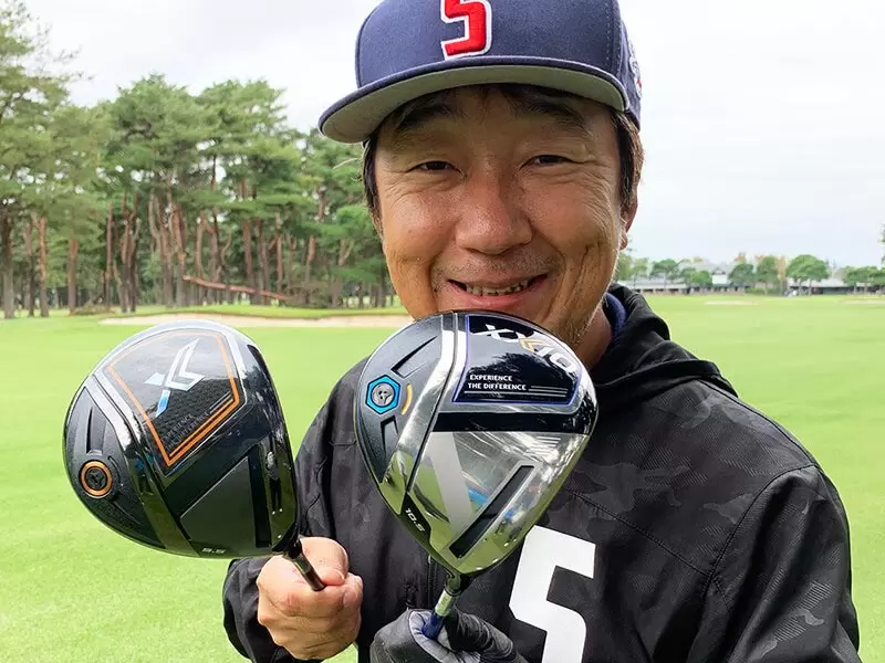 野村タケオが試打したクラブを2本持っている笑顔写真