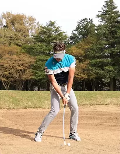 ボールのすぐ手前の砂にバウンスをぶつけるイメージでインパクト。クラブヘッドが鈍角に入っていく。